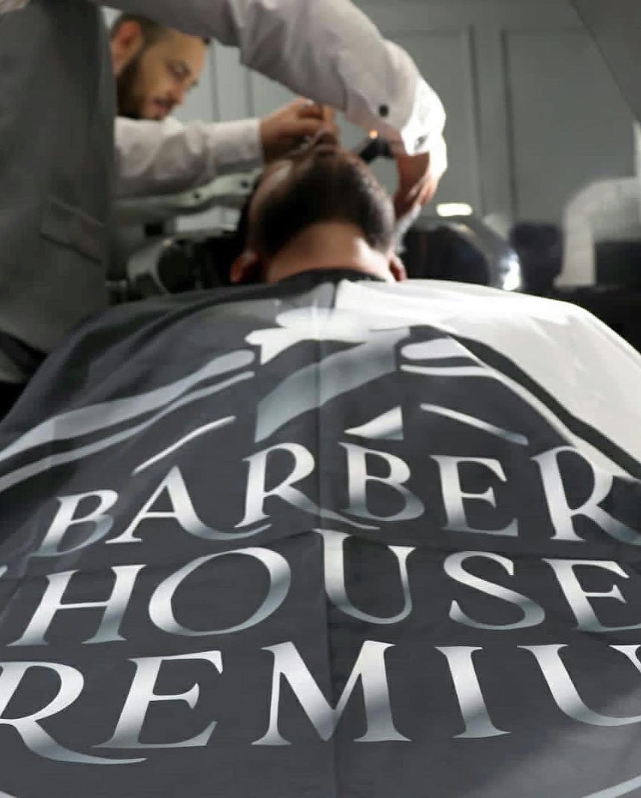 Barbero de Barber House atendiendo a un cliente con capa premium
